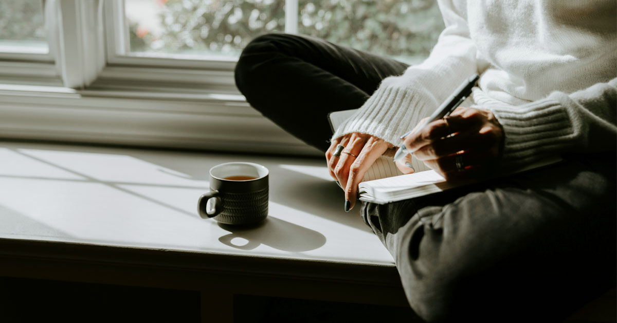 Person journaling beside a cup of tea during a quiet morning routine